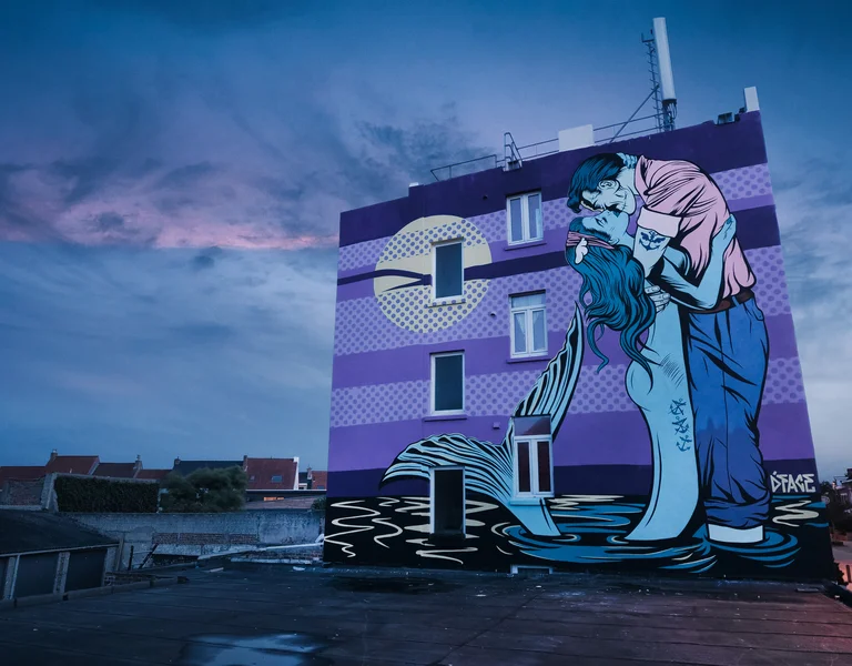 Colorful mural of a man kissing a mermaid on a purple-striped building at dusk.
