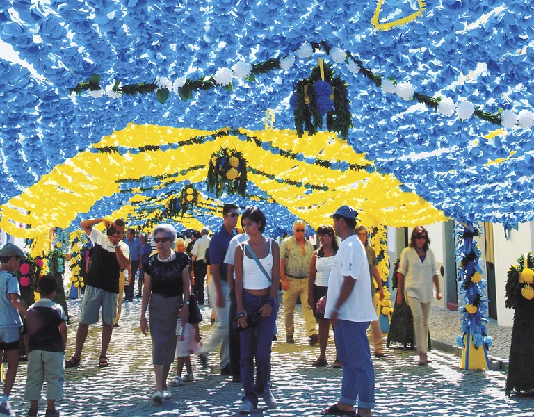 People walk under blue and yellow festival decorations hanging above a street.