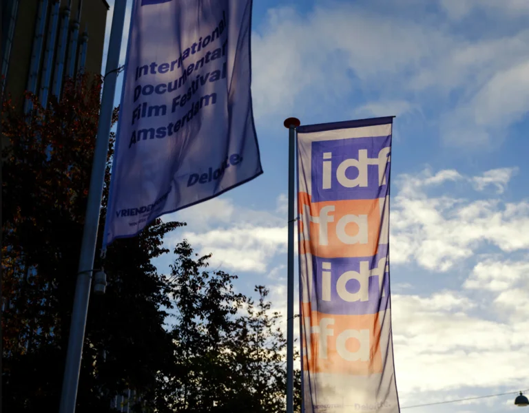Two tall purple banners with "idfa" text, against a partly cloudy sky.