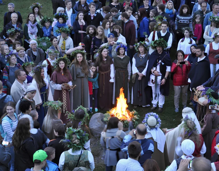 People in traditional clothing gather in a circle around a bonfire outdoors.