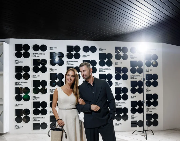 Smiling couple posing together in elegant attire at a modern event with patterned backdrop.
