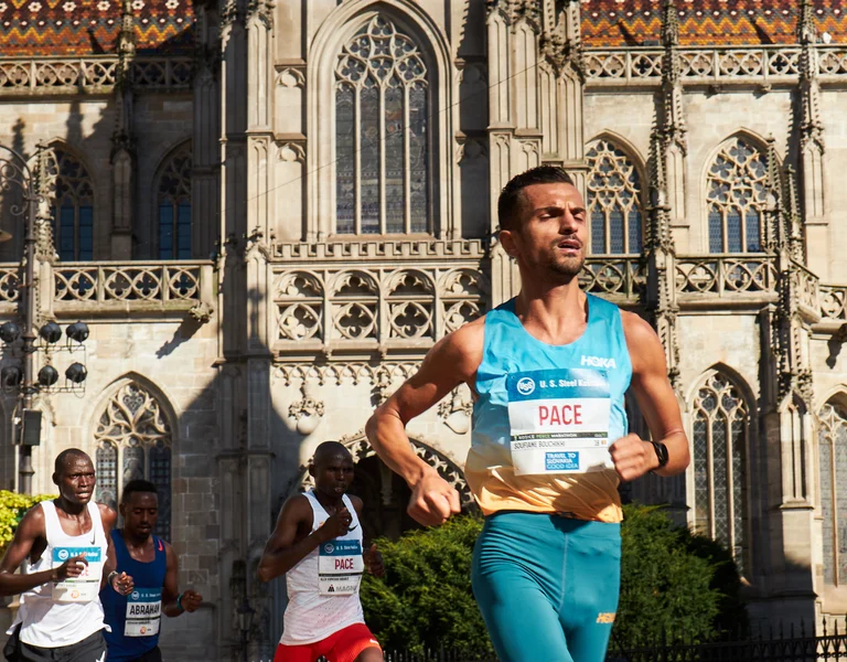Runners competing in a race pass a large historic cathedral on a sunny day.