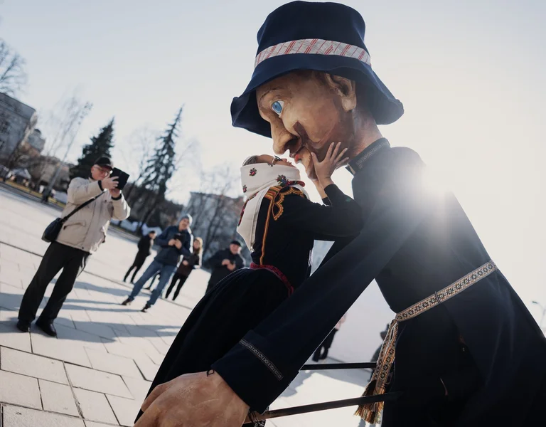 People photographing two large puppets outdoors with sunlight in the background.