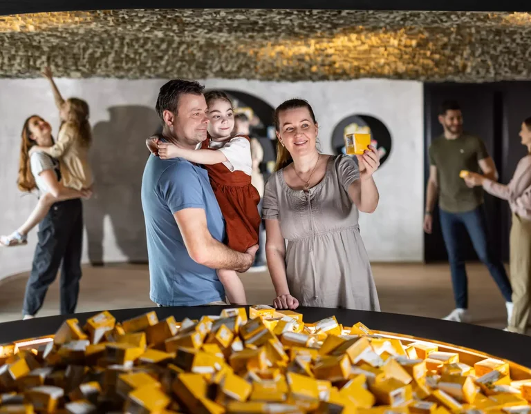 Family smiling near a table of gold bars inside a modern, well-lit exhibit space.