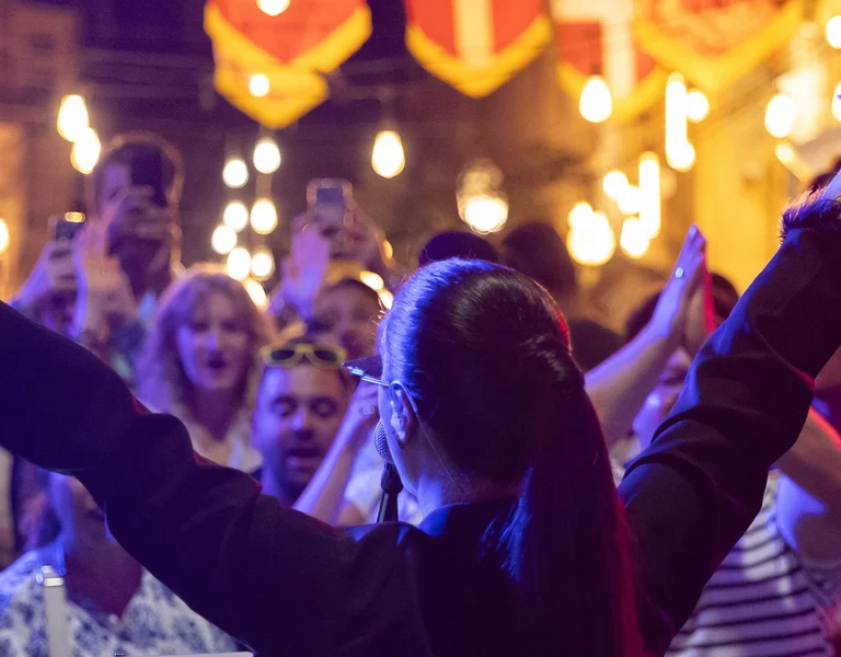 Crowd celebrating at a lively outdoor festival with bright lights and decorations.
