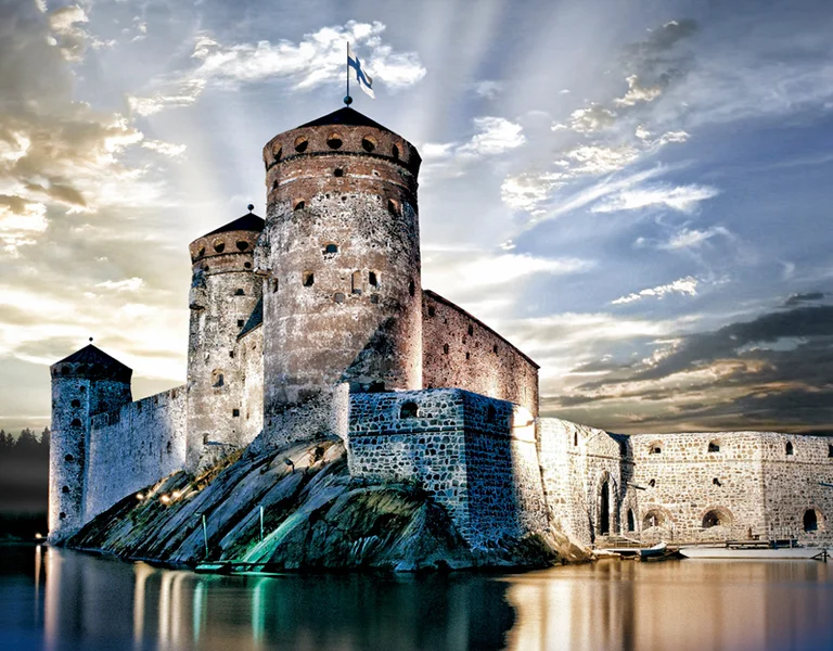 Stone castle with towers reflected in calm water, dramatic sun rays in the sky.