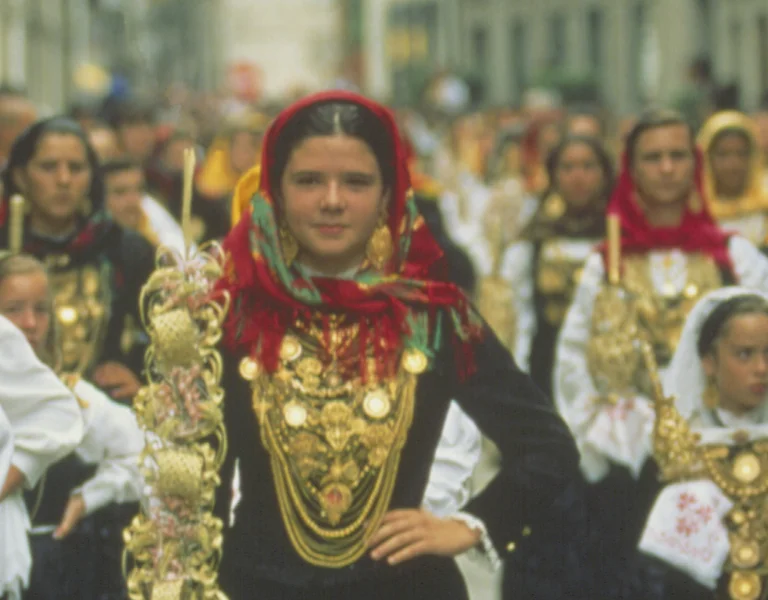 Women in traditional colorful costumes and gold jewelry walking in a festive parade.