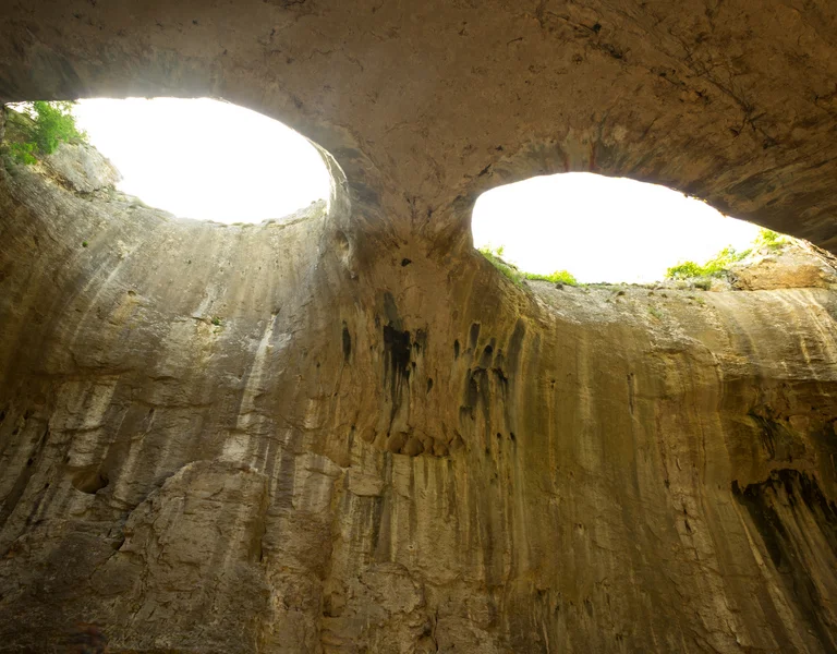 Sunlight beams through two large holes in the roof of a rocky cave.