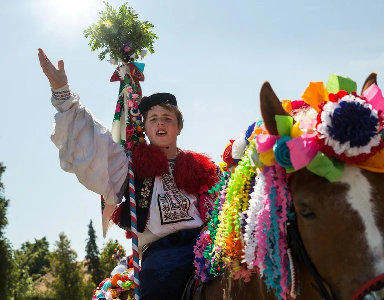 Boy in festive traditional clothing riding a horse decorated with colorful ribbons and flowers.
