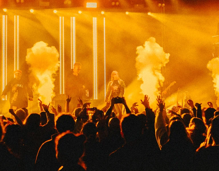 Crowd enjoying a concert with bright orange stage lights and smoke effects.