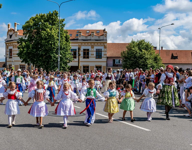 Children in traditional costumes dance in a circle at a street festival, with a crowd watching.