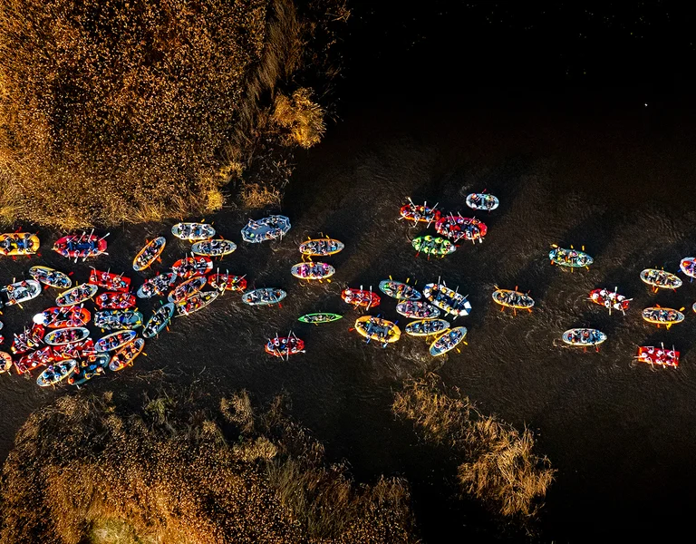 Colorful inflatable rafts floating down a narrow river surrounded by autumn trees.