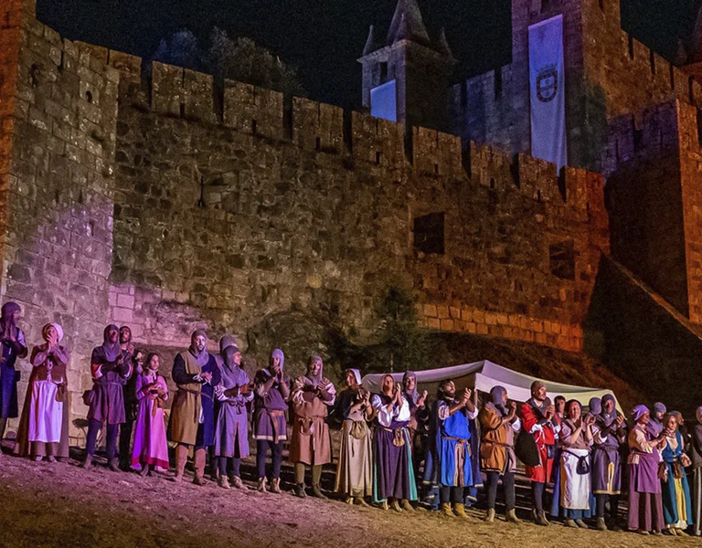 People in medieval costumes stand in front of a brightly lit castle at night.
