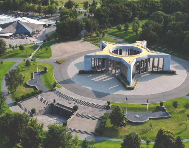Modern circular building with star-shaped roof surrounded by green fields and trees.