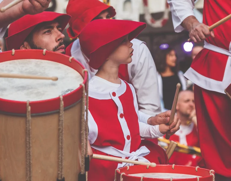 Group of people in red and white costumes playing drums at a parade.