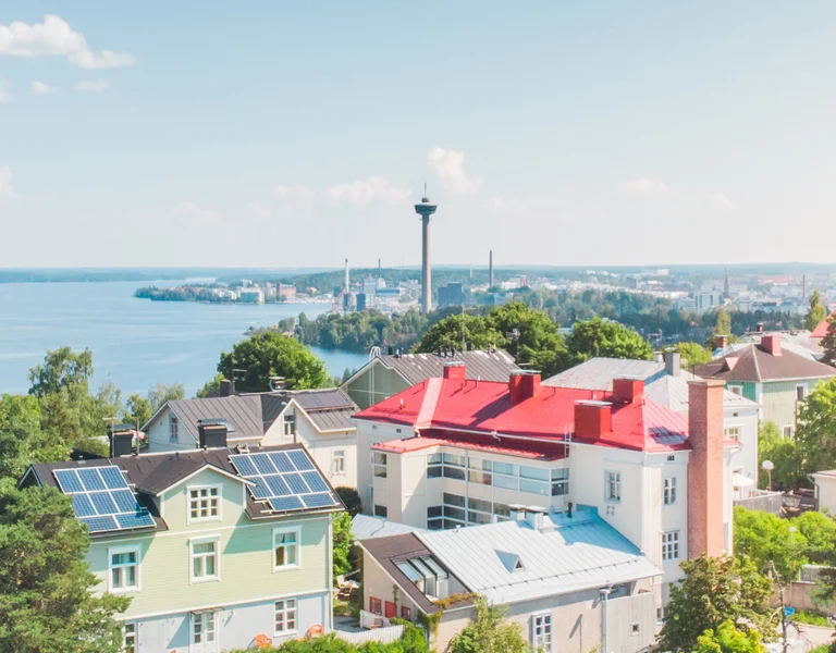 Colorful houses and trees with a lake and city skyline in the background on a sunny day.