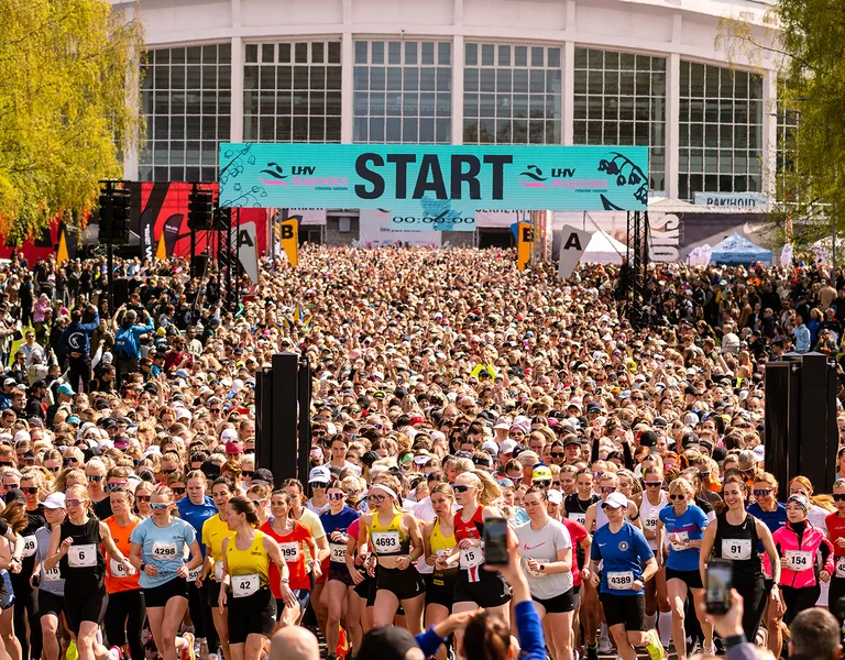 Large crowd of runners at a race starting line surrounded by trees and banners.