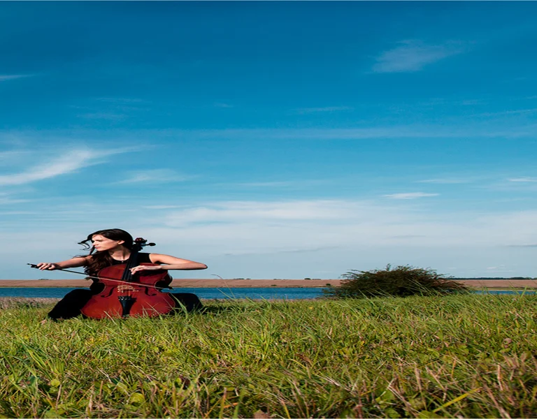 Woman in a red dress running across a grassy field under a blue sky with wispy clouds.