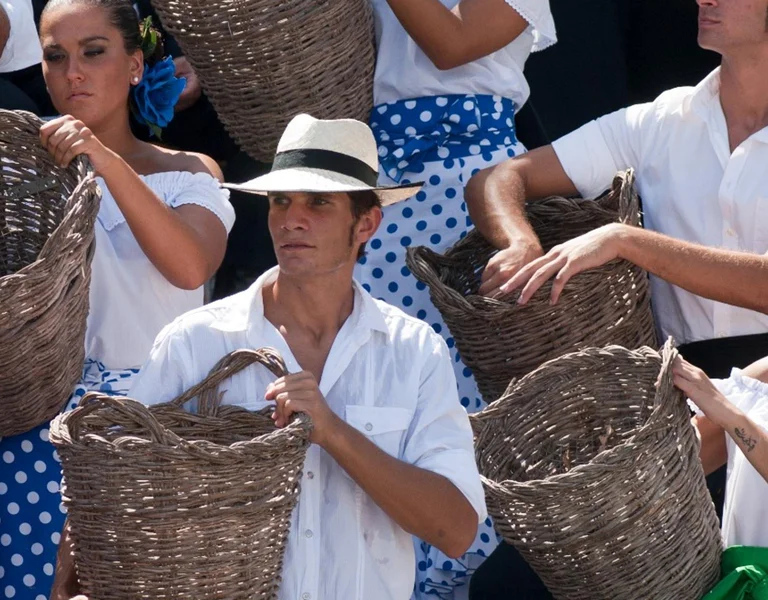 Group of people in traditional clothing holding large wicker baskets outdoors.