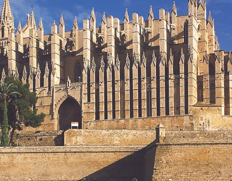 Gothic cathedral with tall spires, fountain in front, clear blue sky.