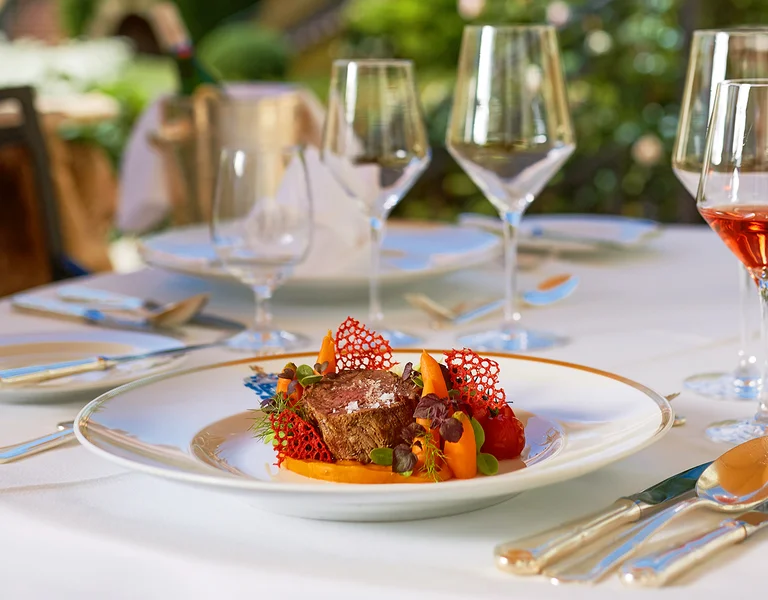 Elegant outdoor dining table set with gourmet meal, wine glasses, and floral centerpiece.