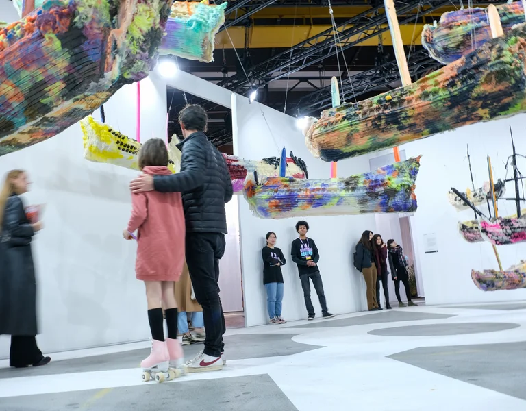 People viewing colorful suspended boat sculptures in a modern art gallery.