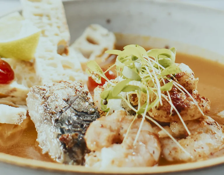 Seafood soup with shrimp, fish, bread slices, lime wedge, and green garnish in a bowl.
