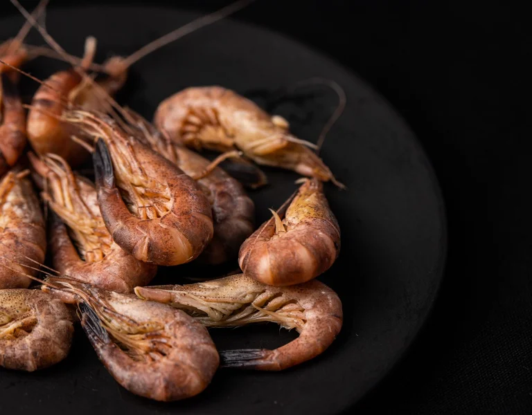 Cooked shrimp piled on a black plate against a dark background.