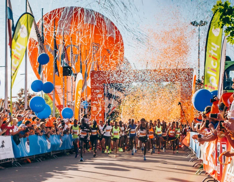 Crowd cheering at the starting line of a colorful outdoor race event with balloons and confetti.