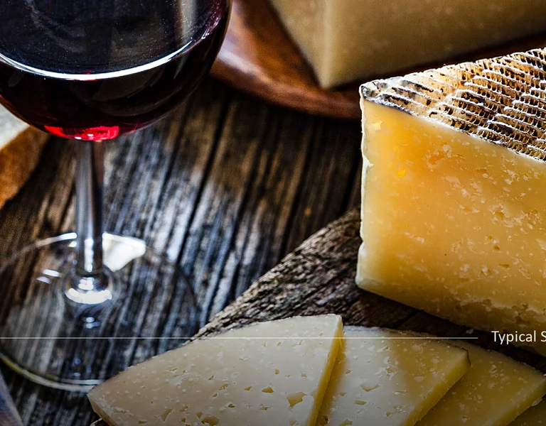 Slices of cheese, cured meats, bread, and a glass of red wine on a rustic wooden table.