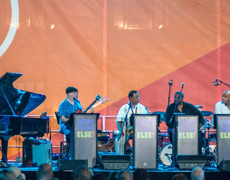Jazz band performing on stage at a festival with audience in the foreground.