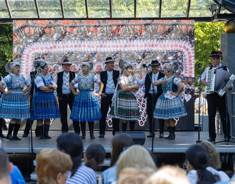 Folk dancers in traditional costumes performing on an outdoor stage before an audience.
