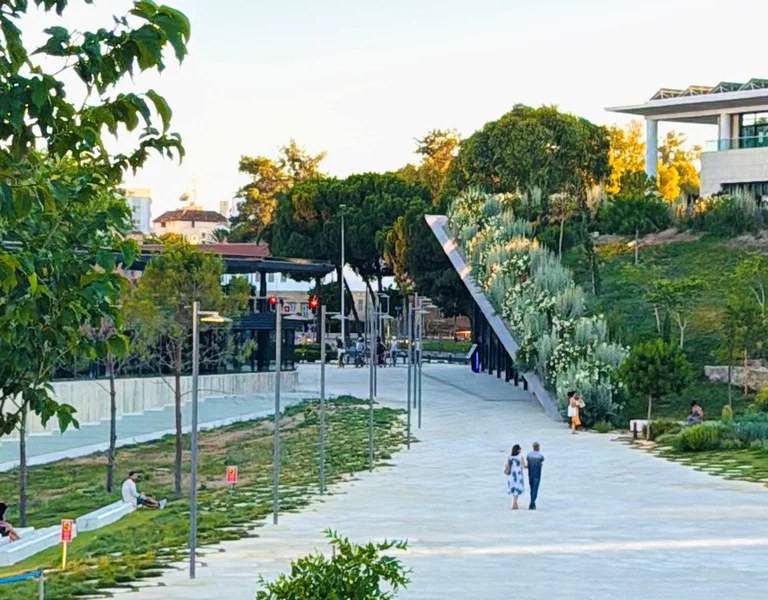 Wide pedestrian pathway lined with trees and modern buildings on a sunny day.