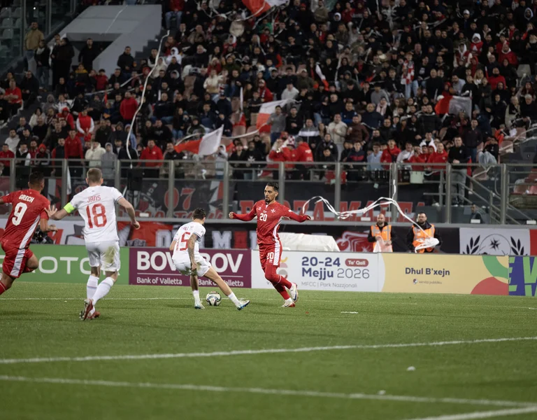 Soccer match in stadium with players in red and white, crowd watching intently.