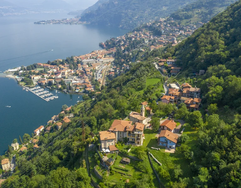 Aerial view of a lakeside town with red-roofed houses and lush green hills.