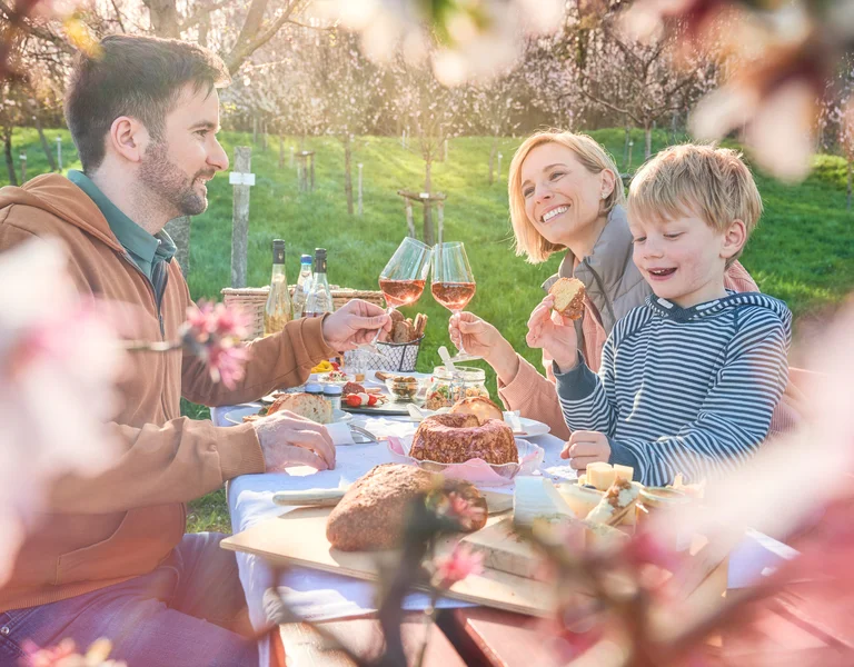 Family enjoying a picnic outdoors surrounded by blooming flowers and sunlight.
