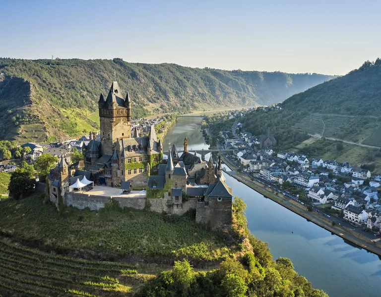 Medieval castle on a hill overlooking a winding river and a small village.