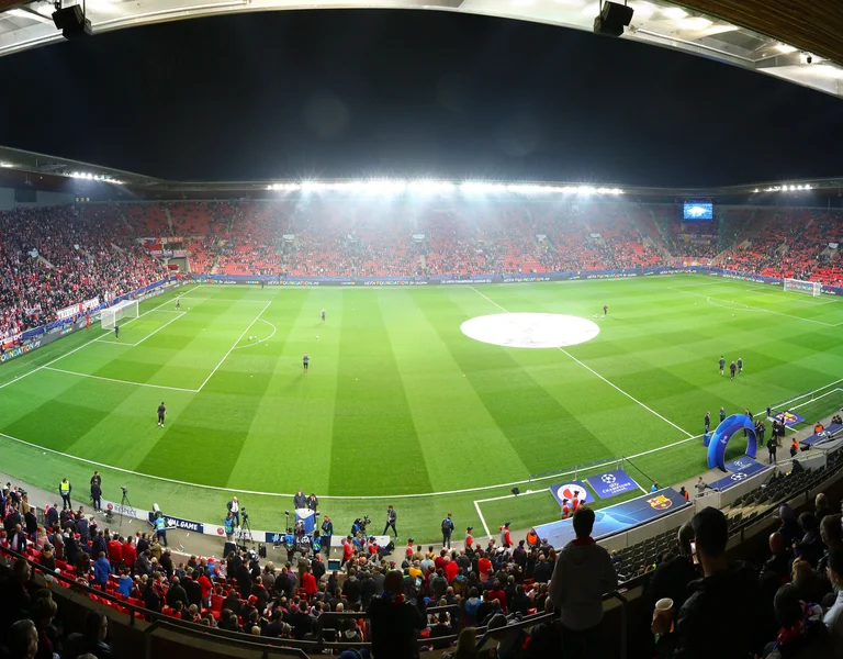 Crowded soccer stadium at night with bright lights and a green field.
