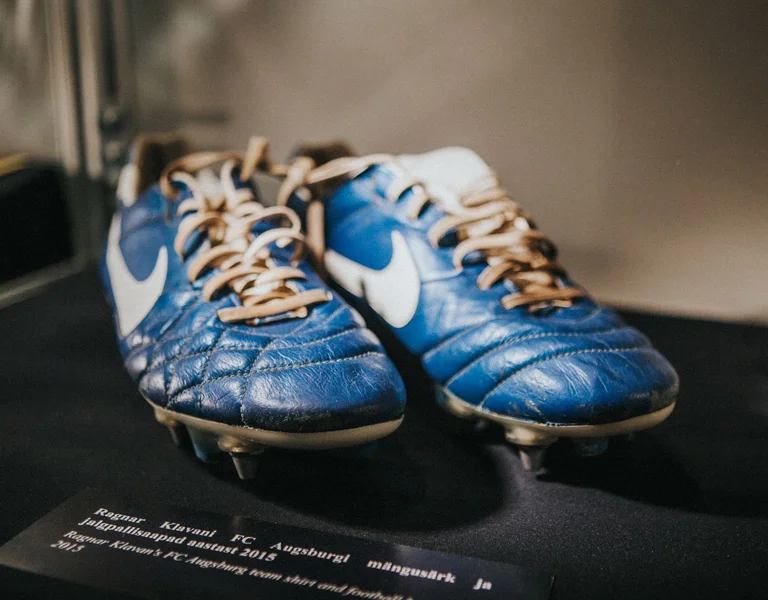 A pair of worn blue Nike soccer cleats displayed on a dark surface.