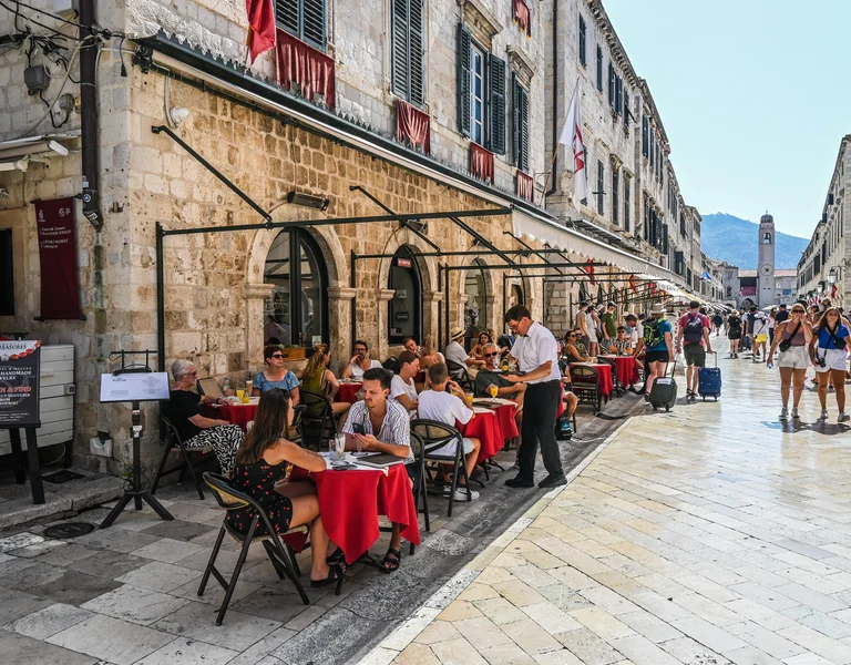 Outdoor café with red tablecloths on a busy street lined with historic stone buildings.
