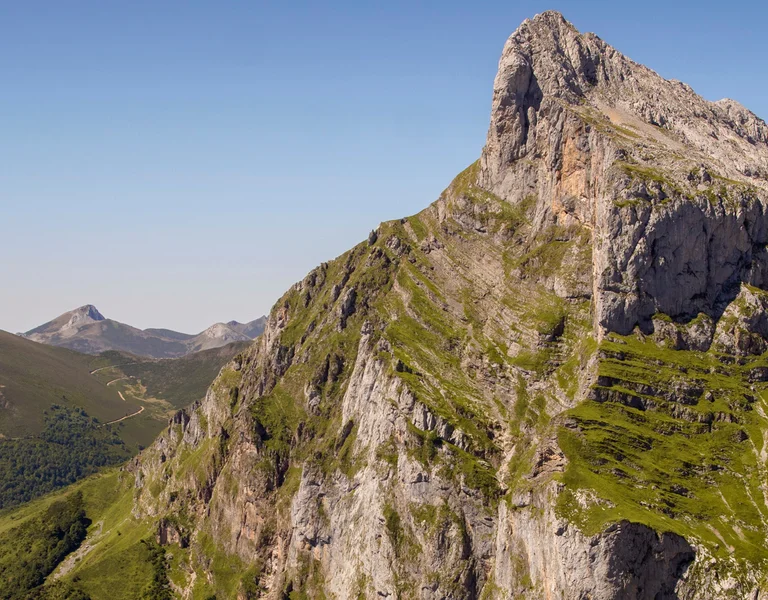 Rocky mountain peaks with green slopes under a clear blue sky.