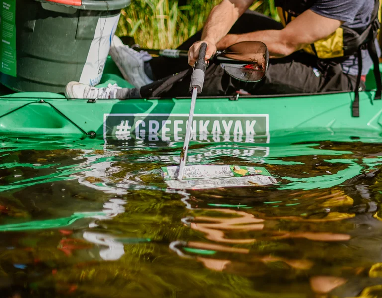 Person collecting trash from the water while sitting in a green kayak.