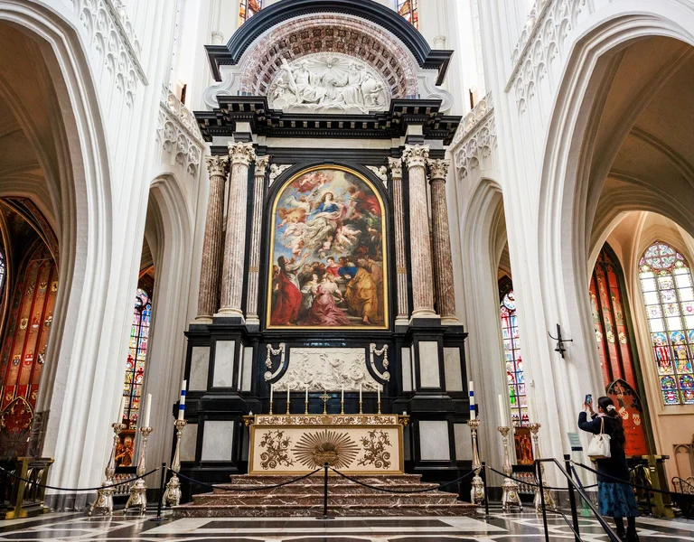 Ornate church altar with a large religious painting, flanked by tall columns and stained glass.