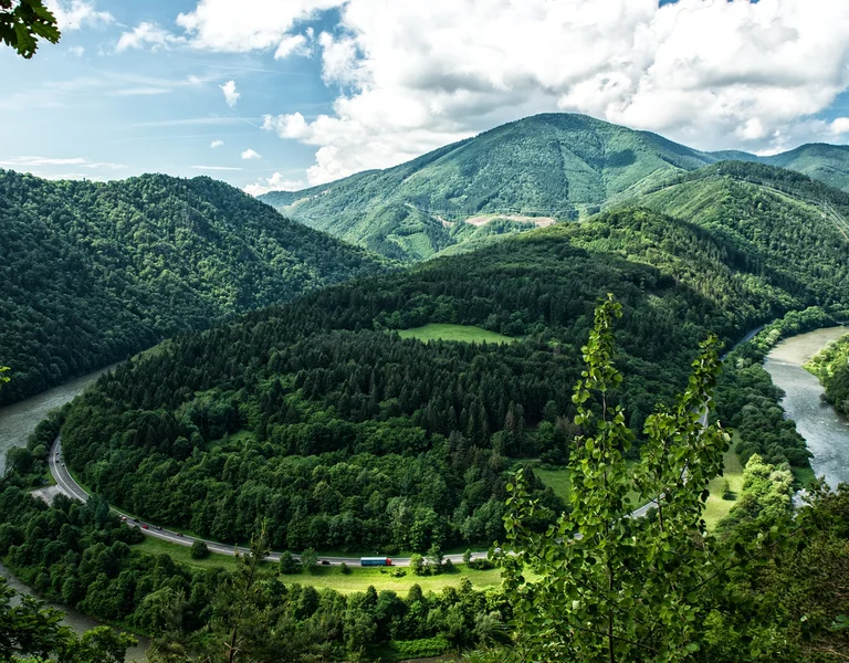 Green mountains with a winding river under a partly cloudy sky.