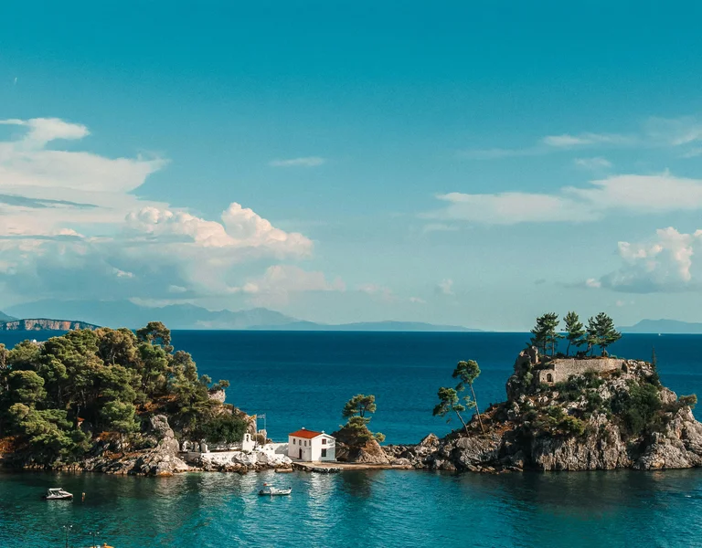 Two small green islands in blue sea under a bright sky with distant clouds.