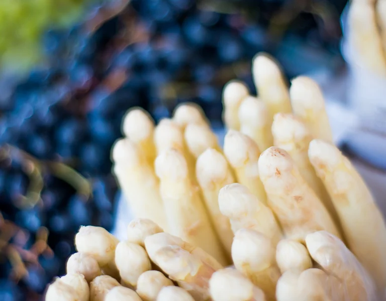 White asparagus spears with dark grapes in the background.