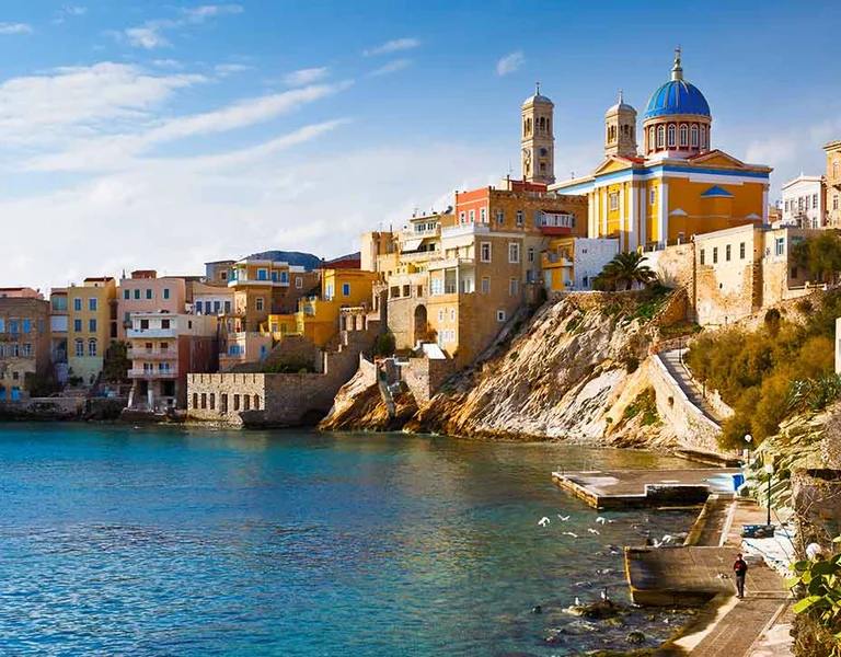 Colorful seaside buildings on a rocky coast with blue water under a clear sky.