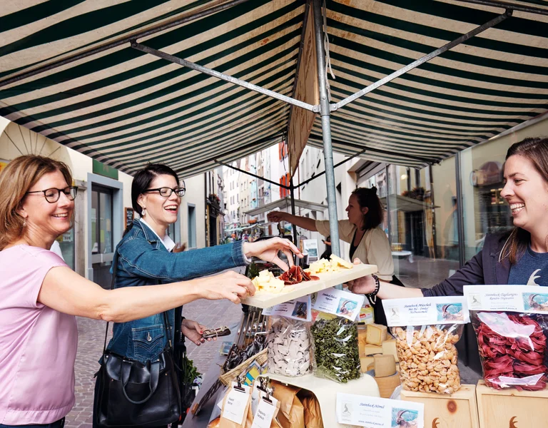 Women smiling while buying dried fruits and nuts at an outdoor market stall.