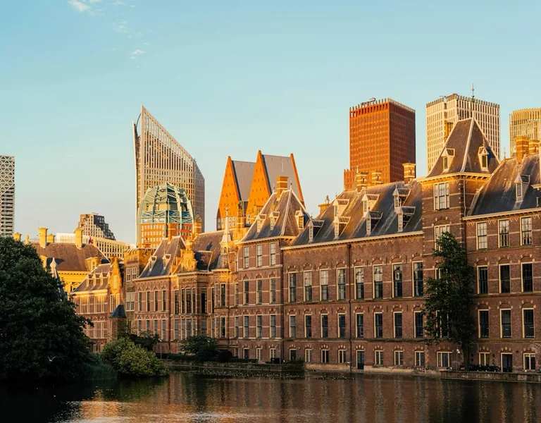 Historic buildings and modern skyscrapers by a canal at sunset.