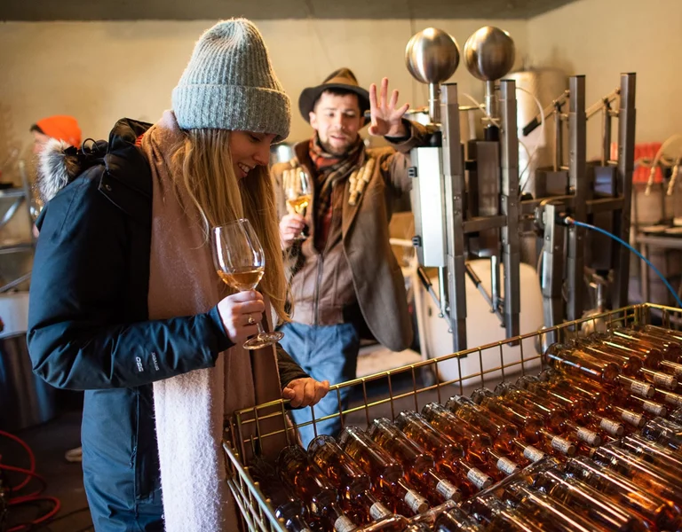 Two people tasting wine in a winery with bottles in the foreground.